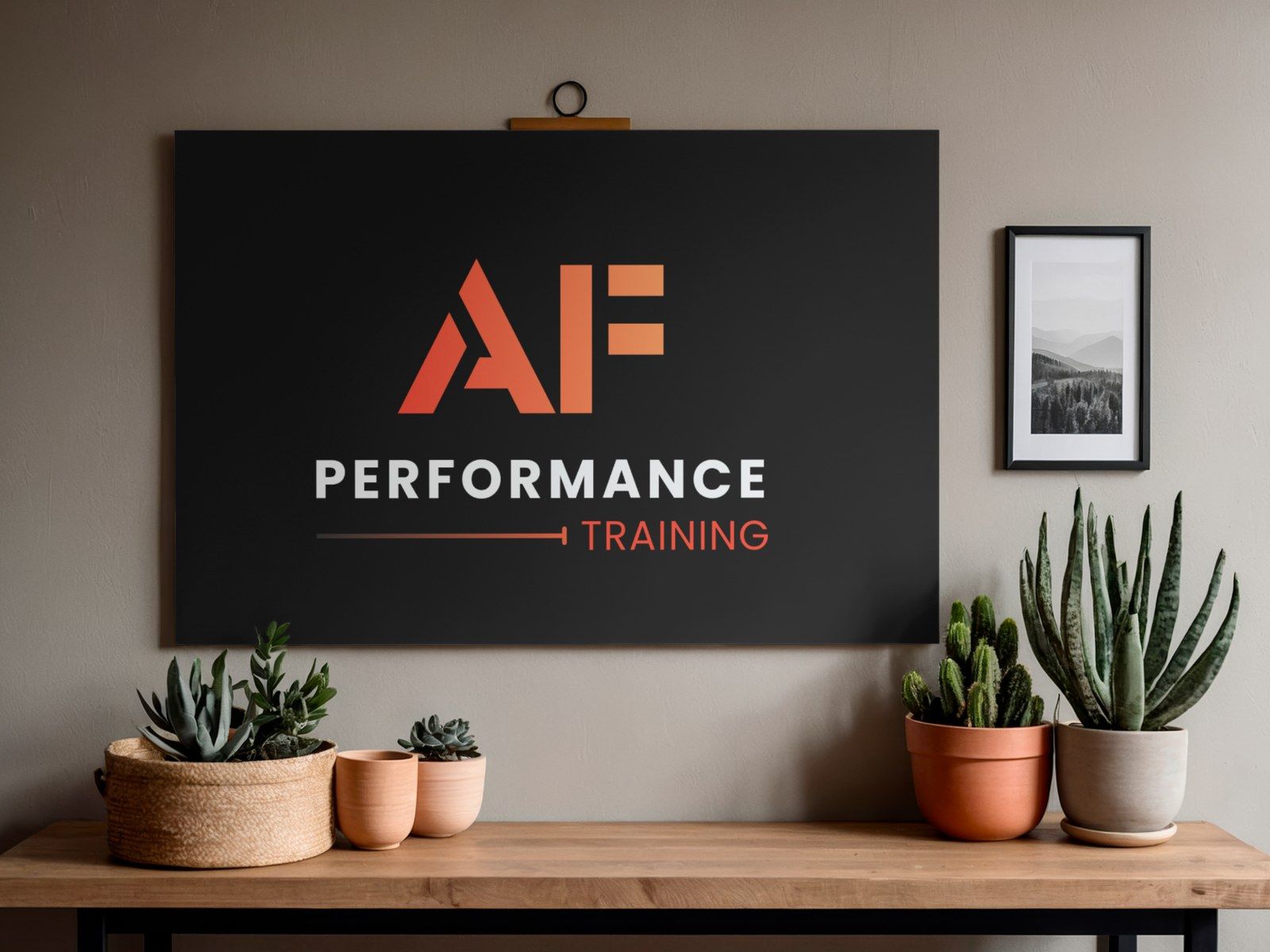 The AF Performance Training logo on a black sign hanging on a wall, above a shelf of potted cacti