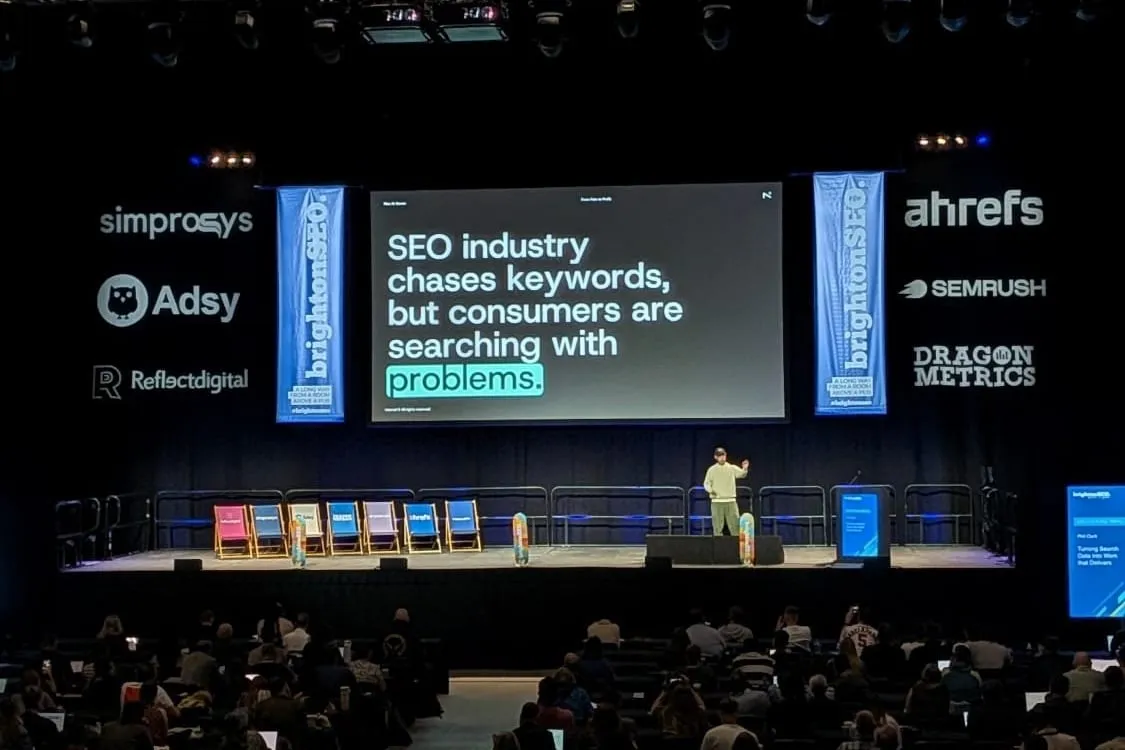 Phil Clark on the brightonSEO main stage, in front of a slide that reads “SEO industry chases keywords, but consumers are searching with problems.”